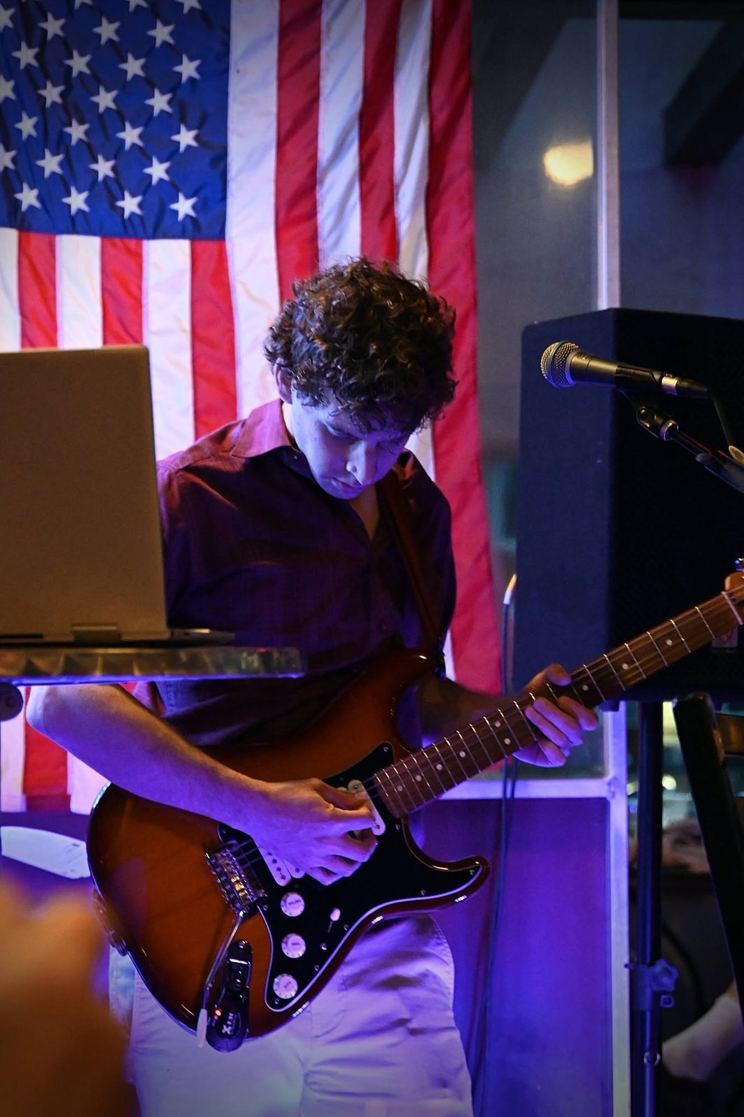 Austin Finnegan looking down at his Stratocaster mid-solo, American flag behind him, at Sierra Madre Saloon