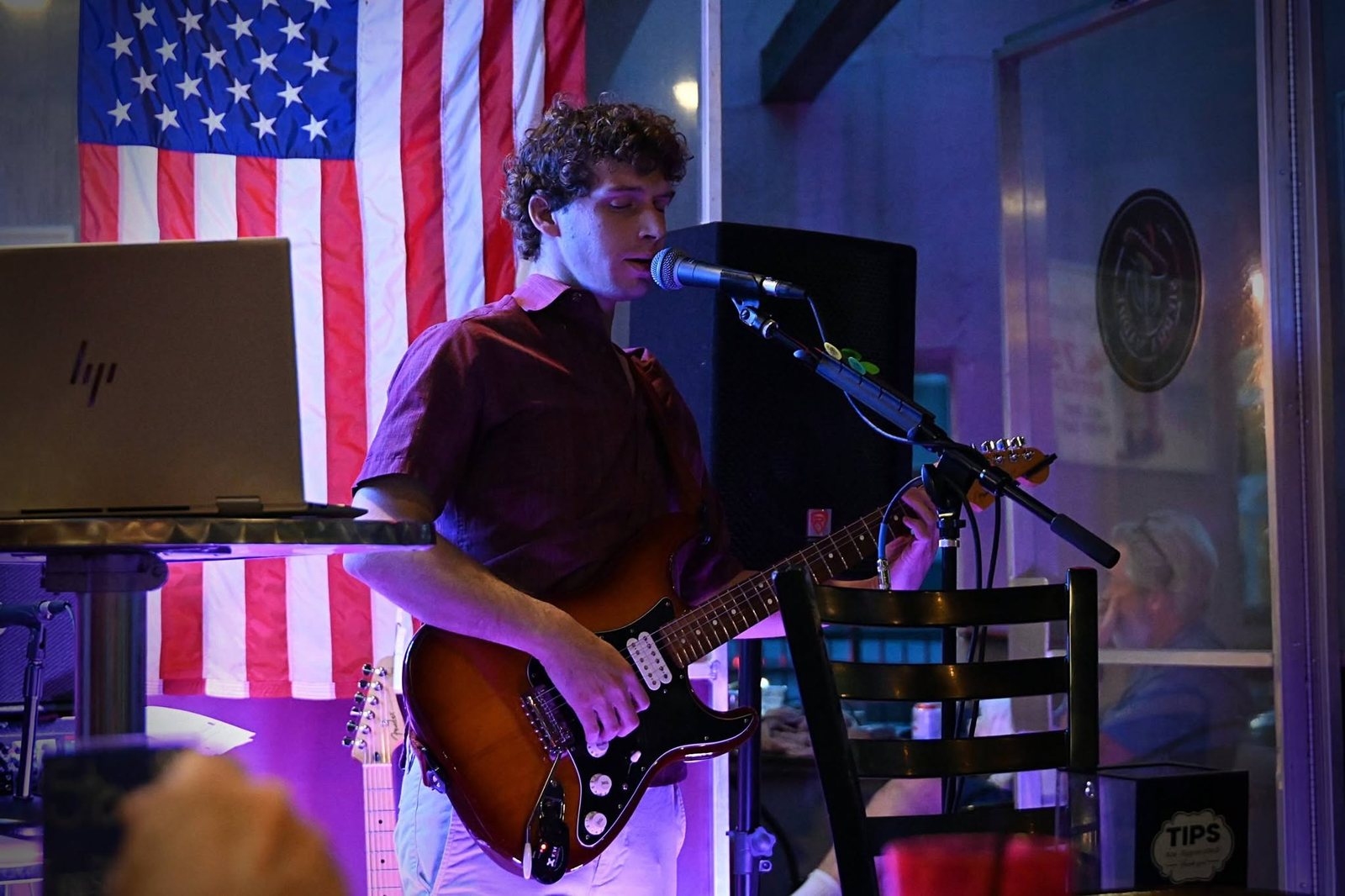 Austin Finnegan at the mic playing his Stratocaster live in front of an American flag at Sierra Madre Saloon